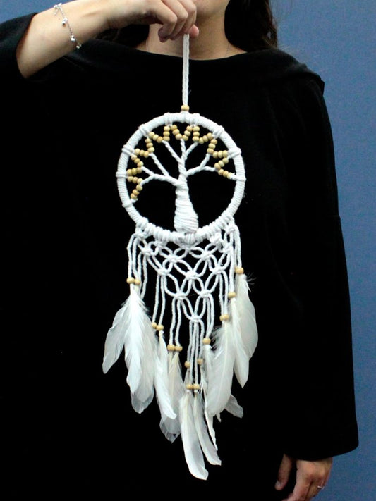 A white macrame dreamcatcher, featuring a tree of life design and white feathers, is held by a person wearing a black shirt.