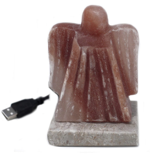 Carved from pink Himalayan salt, an angel-shaped lamp stands on a marble base, accompanied by a USB cord, designed for ambient indoor lighting.