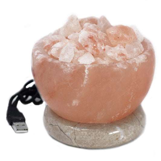 A round pink Himalayan salt bowl containing salt crystals rests atop a polished stone base. A USB cable extends from its side, suggesting electrical functionality.
