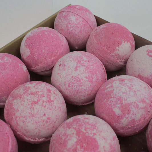 Pink and white speckled bath bombs rest neatly in a cardboard box, indicating preparation for sale or storage in a minimal, neutral setting.