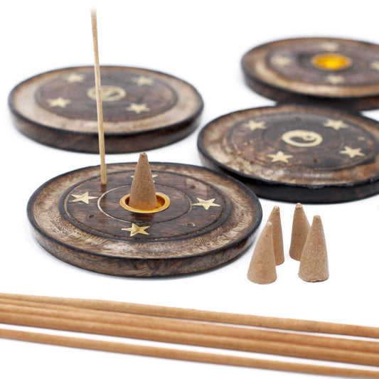 Wooden incense holders display celestial designs with stars and moons. One holder supports a lit incense stick and a cone, surrounded by additional cones and sticks on a white surface.