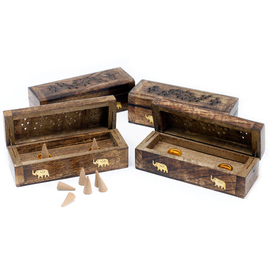 Wooden incense holders, open to reveal incense cones, sit on a white surface. The boxes feature decorative elephant carvings and have perforated lids for fragrance dispersion.