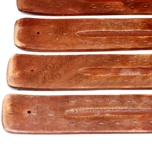 Four wooden incense holders rest parallel, each engraved with floral patterns and small holes. Their smooth, carved surfaces suggest intricate craftsmanship, lying on a white background.