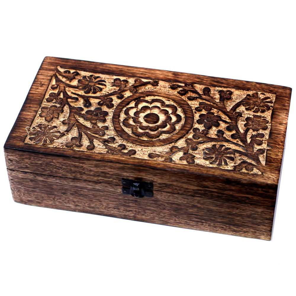 A rectangular, dark-stained wooden box sits in a white space. The lid features carved flowers and leaves, arranged around a circular blossom in the center.