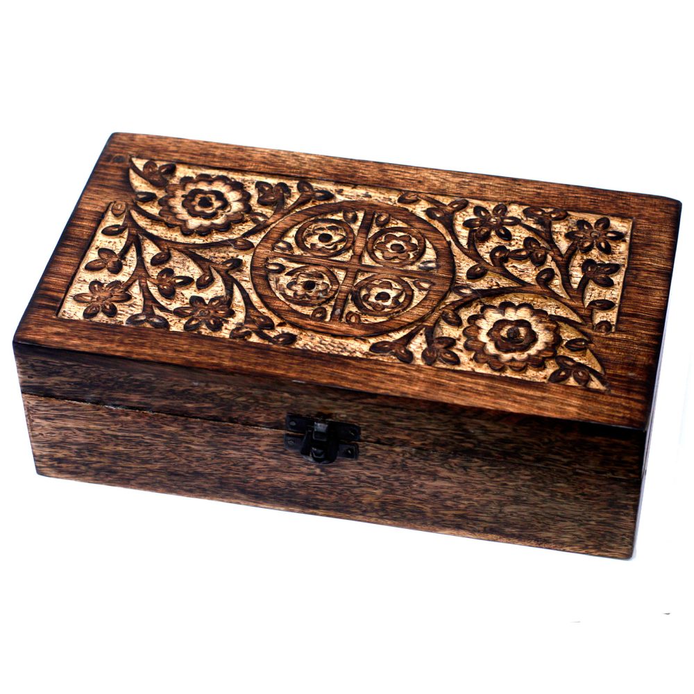 A wooden box is latched closed, sitting on a white surface. The box has a floral design and circular pattern carved into the top.