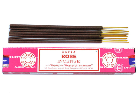 Incense sticks lay next to a pink and white box labeled "SATYA ROSE INCENSE," marked with "EXPORT QUALITY" and "NET. WT. 15 g." It includes an address in Bengaluru, India.