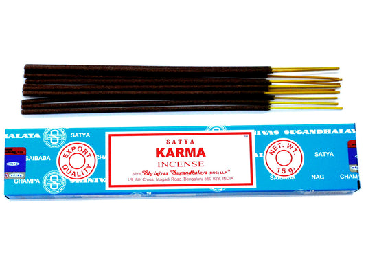 Incense sticks are placed above a blue and red box labeled “SATYA KARMA INCENSE.” The packaging displays "Export Quality" and address details: "Shrinivas Sugandhalaya (BNG) LLP, 1/9, 8th Cross, Magadi Road, Bengaluru-560 023, INDIA.”