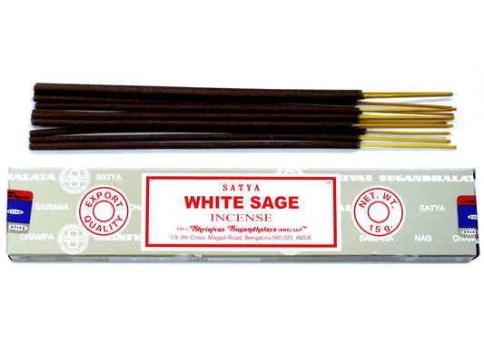 Incense sticks lie on top of a rectangular box labeled "SATYA WHITE SAGE INCENSE." The box features "EXPORT QUALITY" and "NET WT. 15 g" with manufacturer details from Bengaluru, India.