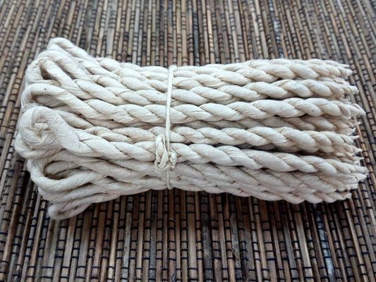A coiled, thick, twisted white rope rests tied with a smaller cord, set against a woven bamboo mat background.