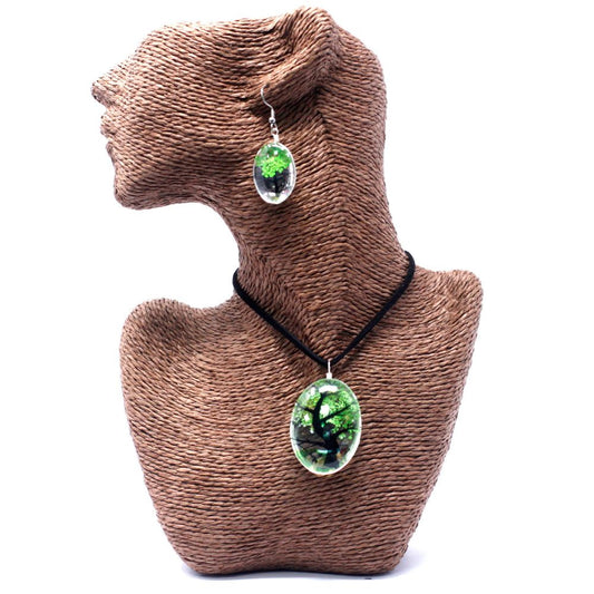 A pendant and earring set, each with a tree encased in clear resin, are displayed on a brown, woven mannequin against a white background.