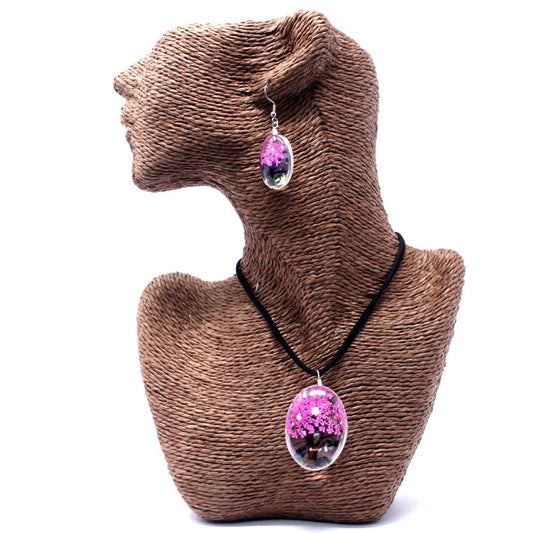 A jewelry set, including a necklace and earring, is displayed on a brown, mannequin bust. The set is oval-shaped, encased in resin, and contains pink flowers.