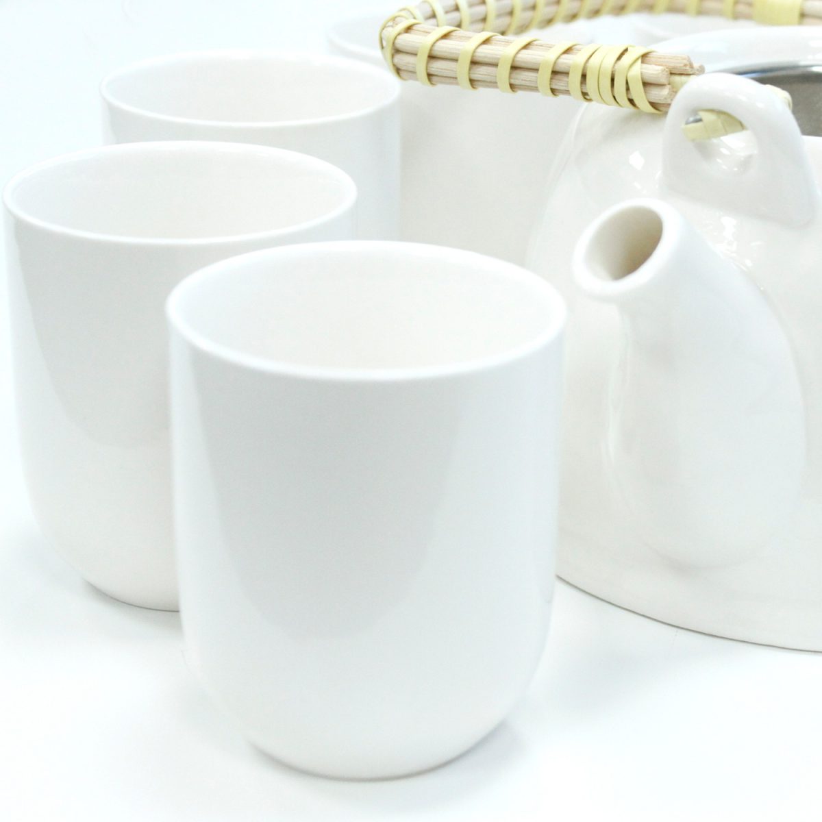 White teacups and a teapot with a woven handle are arranged closely on a white surface, creating a clean, minimalist aesthetic.