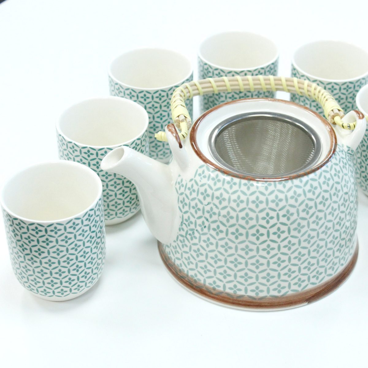 A patterned ceramic teapot with a metal strainer and bamboo handle is surrounded by six matching cups on a white surface.