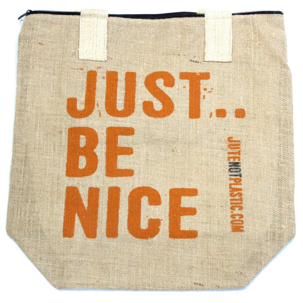 A tan jute tote bag displays the orange text "JUST... BE NICE" vertically, with "JUTENOTPLASTIC.COM" printed vertically in a smaller font beside it. The bag has white woven handles and a black zipper closure.