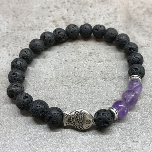 A black, beaded, stretchy bracelet with a silver fish charm and four purple amethyst beads rests on a gray stone surface.