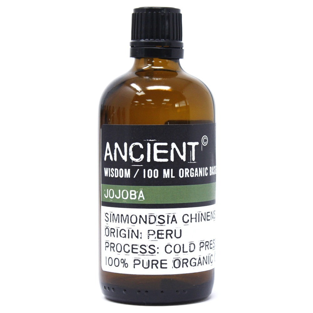 A glass bottle with a black cap stands on a white background. The label reads: "ANCIENT. WISDOM / 100 ML ORGANIC BASE. JOJOBA. SIMMONDSIA CHINENS. ORIGIN: PERU. PROCESS: COLD PRES. 100% PURE ORGANIC."