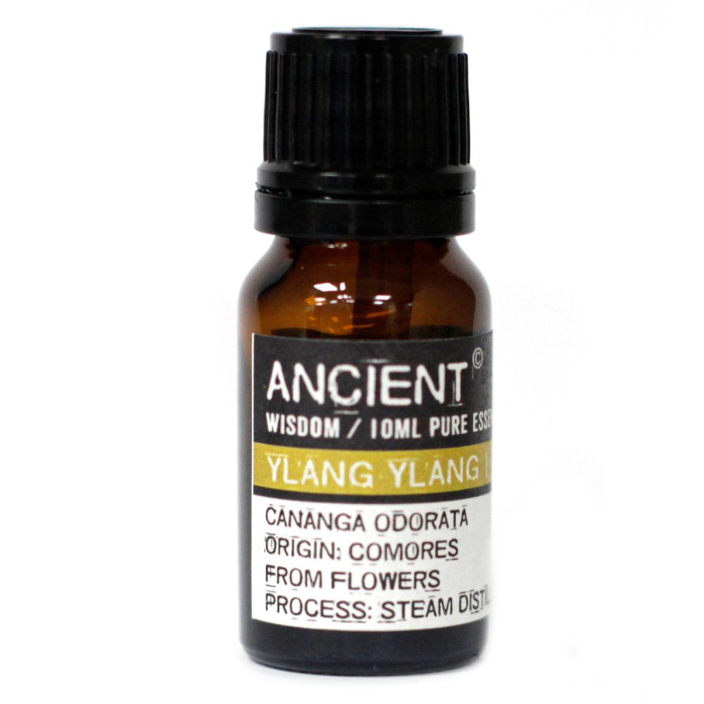 A small amber bottle with a black cap sits on a white surface. It is labeled "ANCIENT WISDOM / 10ML PURE ESS YLANG YLANG CANANGA ODORATA ORIGIN: COMORES FROM FLOWERS PROCESS: STEAM DIST."