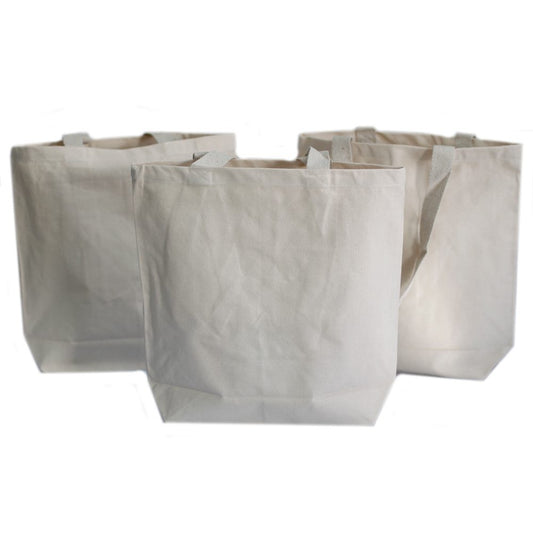 Three canvas tote bags stand upright in a row on a white surface. The bags are a light, unbleached color and have short handles.