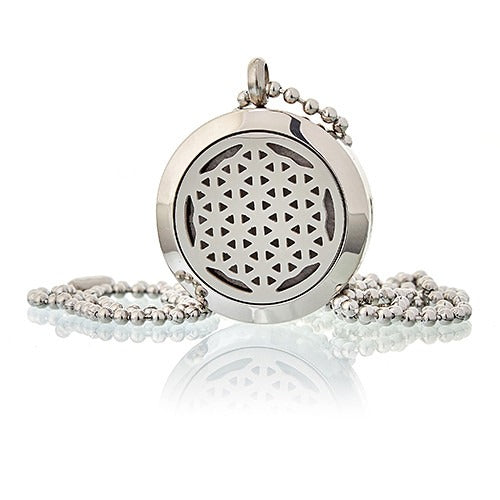 A silver locket with a triangle pattern sits on a beaded chain, reflecting off a white surface.