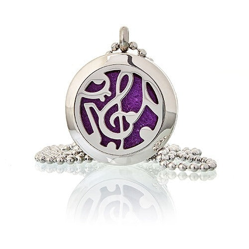 A silver, circular pendant with a cutout treble clef is attached to a beaded chain, reflecting light on a white surface. Purple felt is visible behind the cutout.