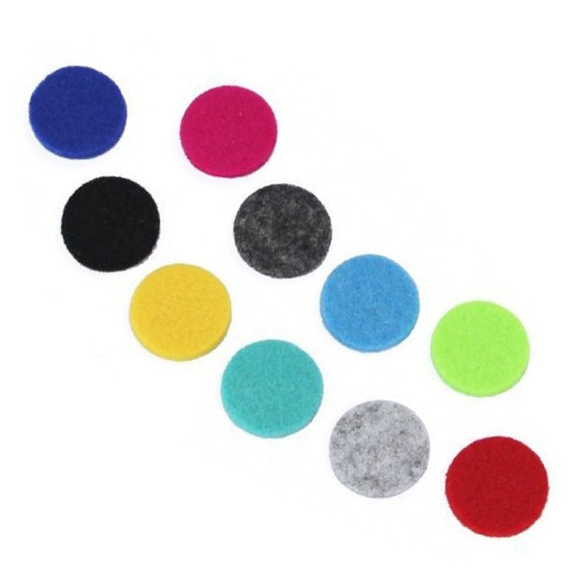 Ten circular, colorful felt pads are arranged on a white surface in a diagonal row. The colors include blue, pink, black, gray, yellow, and various shades of turquoise, green, and red.
