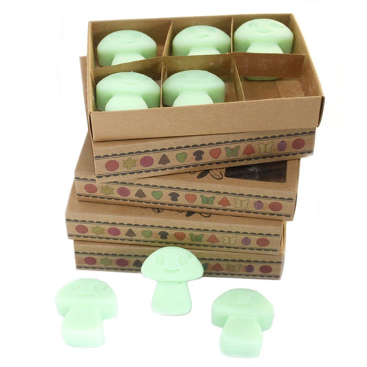 Pale green mushroom-shaped wax melts are stacked in cardboard boxes with decorative borders. Three additional melts sit in front.