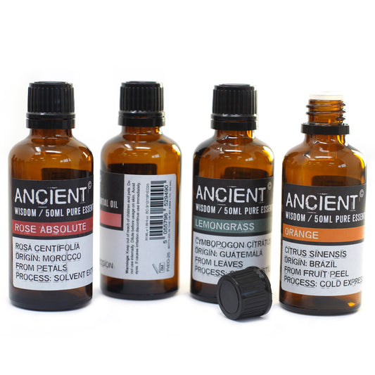 Four amber bottles, labeled "ANCIENT WISDOM / 50ML PURE ESSEN," stand on a white surface. From left to right, the bottles are labeled, "ROSE ABSOLUTE," "LEMONGRASS," and "ORANGE." A black bottle cap lays to the side of the lemongrass bottle.