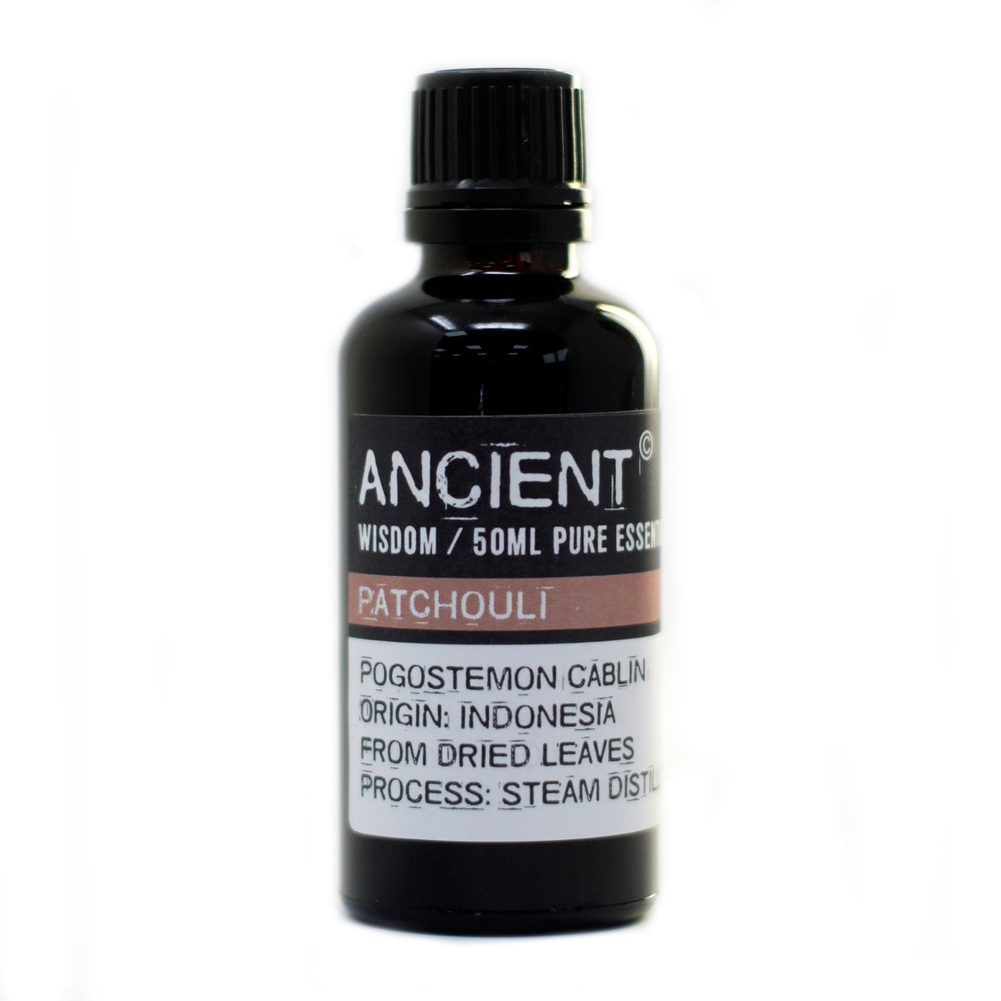 A dark brown glass bottle of “ANCIENT” brand essential oil sits on a white surface. The label reads "WISDOM / 50ML PURE ESSEN", "PATCHOULI", "POGOSTEMON CABLIN", "ORIGIN: INDONESIA", "FROM DRIED LEAVES", and "PROCESS: STEAM DISTIL".