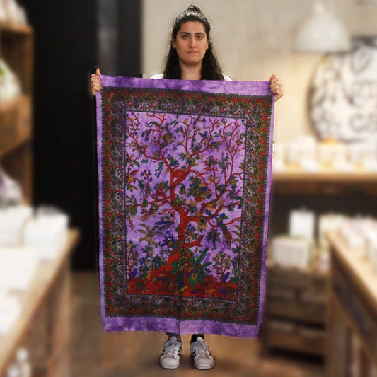 A woman holds a purple tapestry depicting a tree of life. The tapestry is detailed with birds and flowers. The scene is a shop.
