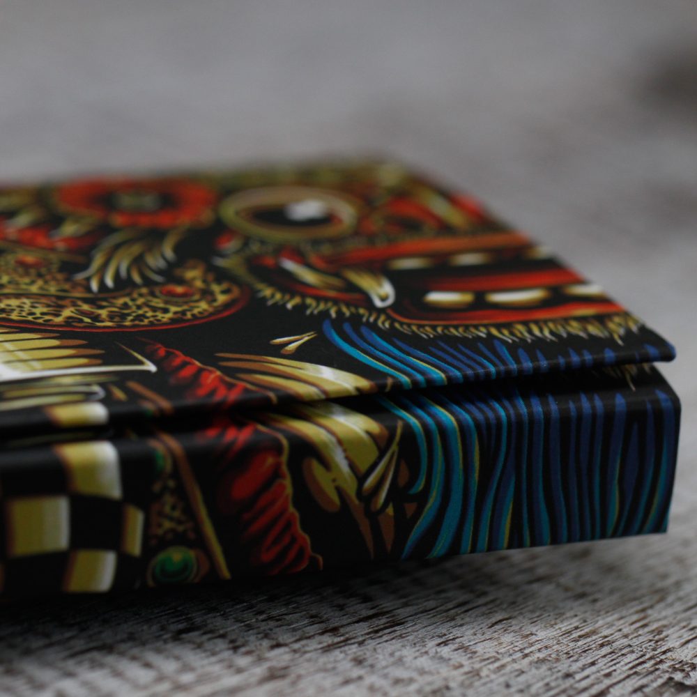 A rectangular box sits on a textured surface. The box has a vibrant design with black, gold, red, and blue colors.