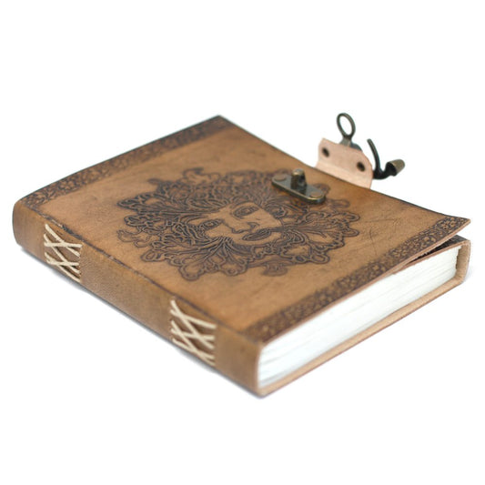 A tan leather journal with a clasp rests closed against a white backdrop, its cover embossed with a leafy human face. Its spine is stitched with white threads.