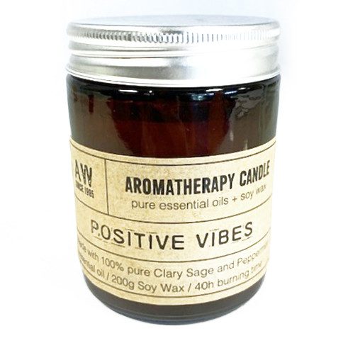 A brown aromatherapy candle jar with a silver lid sits in a white space. Text on its label reads "AROMATHERAPY CANDLE pure essential oils + soy wax POSITIVE VIBES made with 100% pure Clary Sage and Peppermint essential oil/200g Soy Wax/40h burning time."