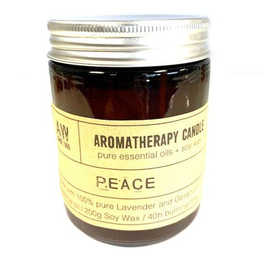 A brown glass jar candle with a silver lid features a beige label. "AW, AROMATHERAPY CANDLE, pure essential oils + soy wax, PEACE, Made with 100% pure Lavender and Geranium essential oil / 200g Soy Wax / 40h burning time."