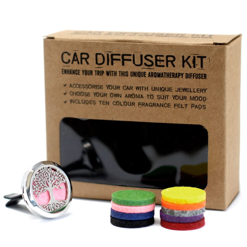 The "Car Diffuser Kit" box sits behind a silver diffuser clip with a "tree of life" design and pink felt pad. Stacks of colorful fragrance felt pads sit beside the kit box. Text on the box reads: "CAR DIFFUSER KIT ENHANCE YOUR TRIP WITH THIS UNIQUE AROMATHERAPY DIFFUSER ✔ ACCESSORISE YOUR CAR WITH UNIQUE JEWELLERY ✓ CHOOSE YOUR OWN AROMA TO SUIT YOUR MOOD ✓ INCLUDES TEN COLOUR FRAGRANCE FELT PAD'S"