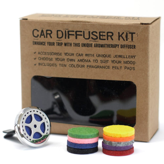A car diffuser kit box stands behind a silver diffuser with a blue felt pad and two small stacks of colored felt pads. The box reads: "CAR DIFFUSER KIT ENHANCE YOUR TRIP WITH THIS UNIQUE AROMATHERAPY DIFFUSER \✓ ACCESSORISE YOUR CAR WITH UNIQUE JEWELLERY \✓ CHOOSE YOUR OWN AROMA TO SUIT YOUR MOOD \✓ INCLUDES TEN COLOUR FRAGRANCE FELT PAD'S"
