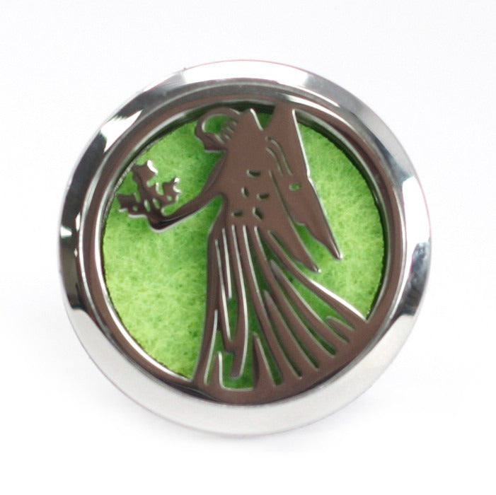 A silver round pendant displays an angel silhouette holding a flower bouquet, against a bright green textured backdrop. The pendant rests on a white surface.
