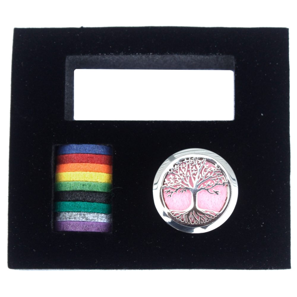 A silver locket, displaying a tree design with pink background, sits alongside a stack of rainbow-colored felt pads, within a black velvet box.