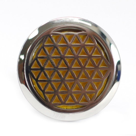 A round, silver diffuser is centered in the frame, displaying a 'Flower of Life' pattern over a yellow felt pad, against a white background.