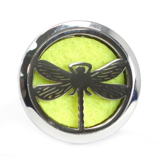 A silver dragonfly design sits atop a round, yellow, porous pad, all encased within a smooth, silver, circular frame, set against a white background.