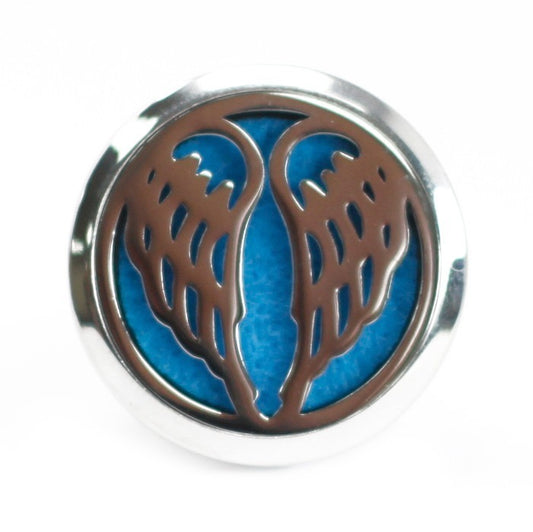 A round, metal locket displays stylized metal-cut angel wings against a blue felt background, set against a white surface.
