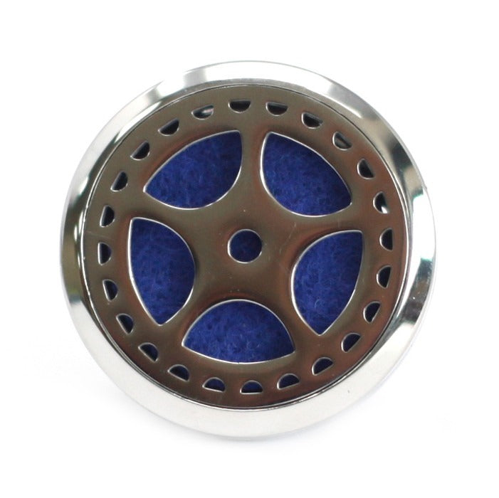 A round, silver locket-style pendant features a five-spoked design over a textured, dark blue pad. The object is displayed on a stark white surface.