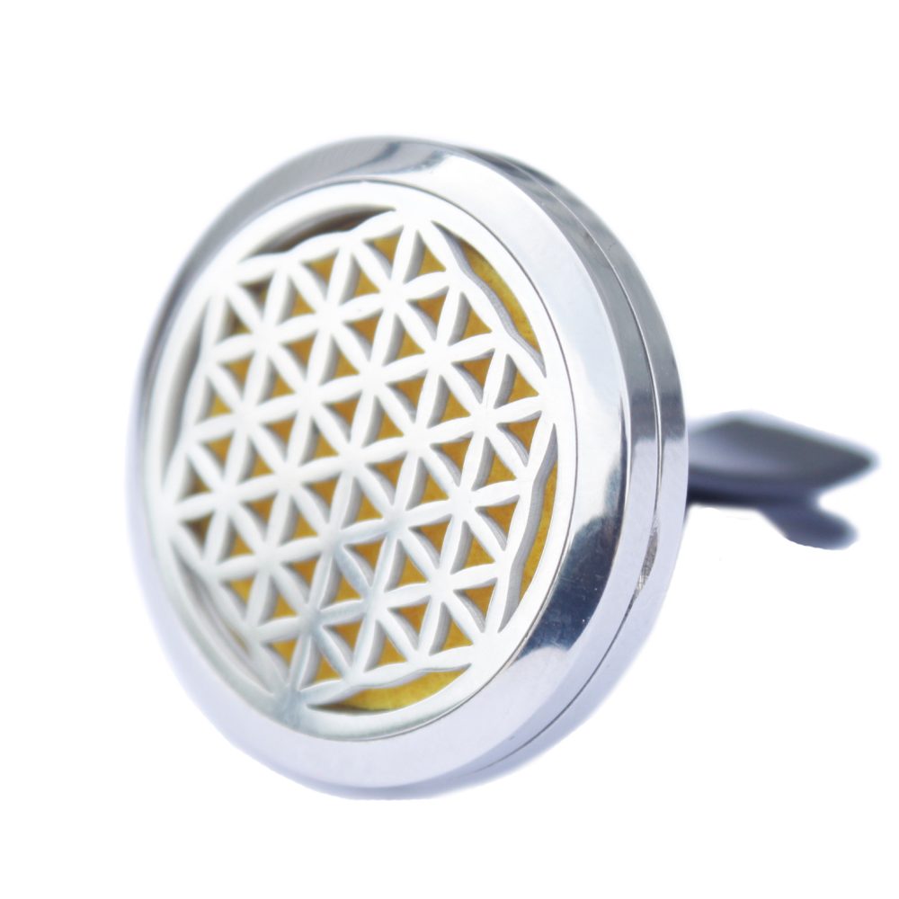 The circular, silver air freshener shows a geometric pattern with a yellow interior. The gray vent clip is angled to the right on a white background.