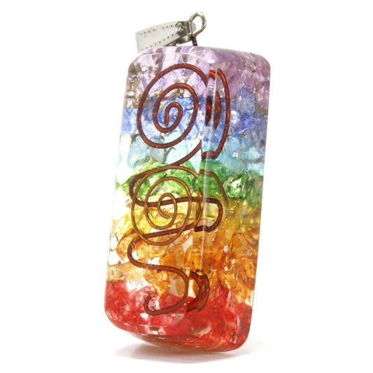 A rectangular pendant, filled with crushed stones in rainbow colors, features a looped copper wire design. The pendant is hanging against a white background.