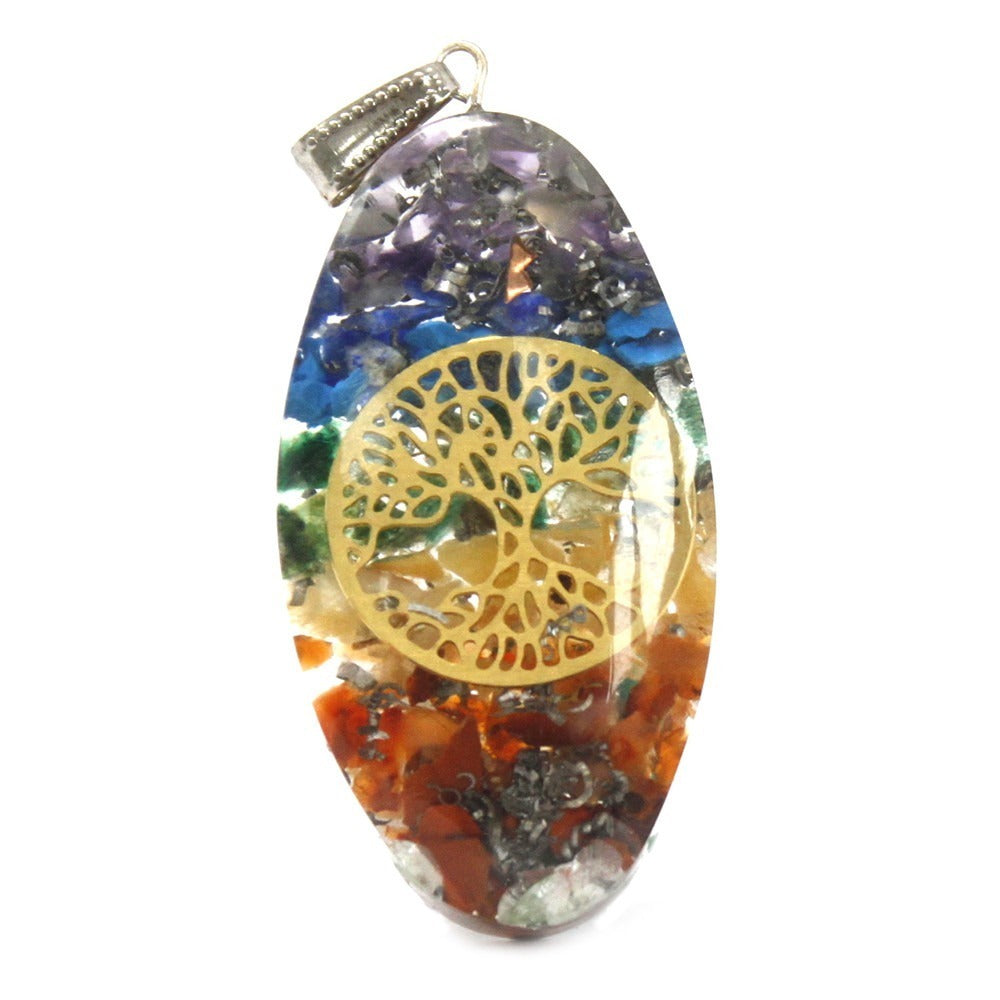 A pendant, with a silver loop, shows layered, colorful stones and metal pieces encased in clear resin. A gold-colored tree is placed on the pendant's center. It rests on a white background.