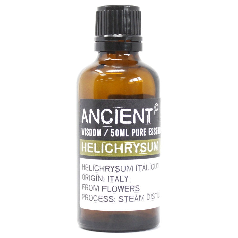 A brown glass bottle stands on a white surface. The label reads "ANCIENT WISDOM / 50ML PURE ESSENCE HELICHRYSUM HELICHRYSUM ITALICUM ORIGIN: ITALY FROM FLOWERS PROCESS: STEAM DISTIL".