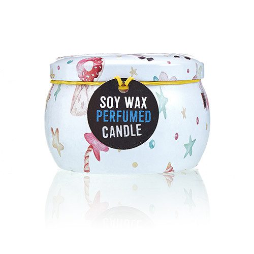 A small round decorative tin candle sits on a reflective white surface, patterned with pastel seashells and stars; label reads "SOY WAX PERFUMED CANDLE".