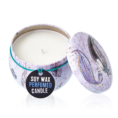 Round decorative tin candle sits open with unlit wick, lid propped aside; illustrated mermaid motifs and teal elastic band on white background, black tag reading SOY WAX PERFUMED CANDLE