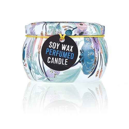 A floral-patterned candle jar sits on a reflective surface. A yellow band wraps around the top, securing a black tag which reads "SOY WAX PERFUMED CANDLE."