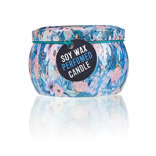 A candle sits against a white background, reflecting light. The floral-patterned, rounded metal container is labeled "SOY WAX PERFUMED CANDLE" on a black tag hanging from the top.
