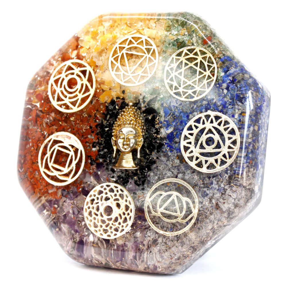 Orgone pyramid displays a small, gold-colored Buddha statue surrounded by several geometric symbols over layered colorful crystals in an octagonal shape, isolated on a white background.